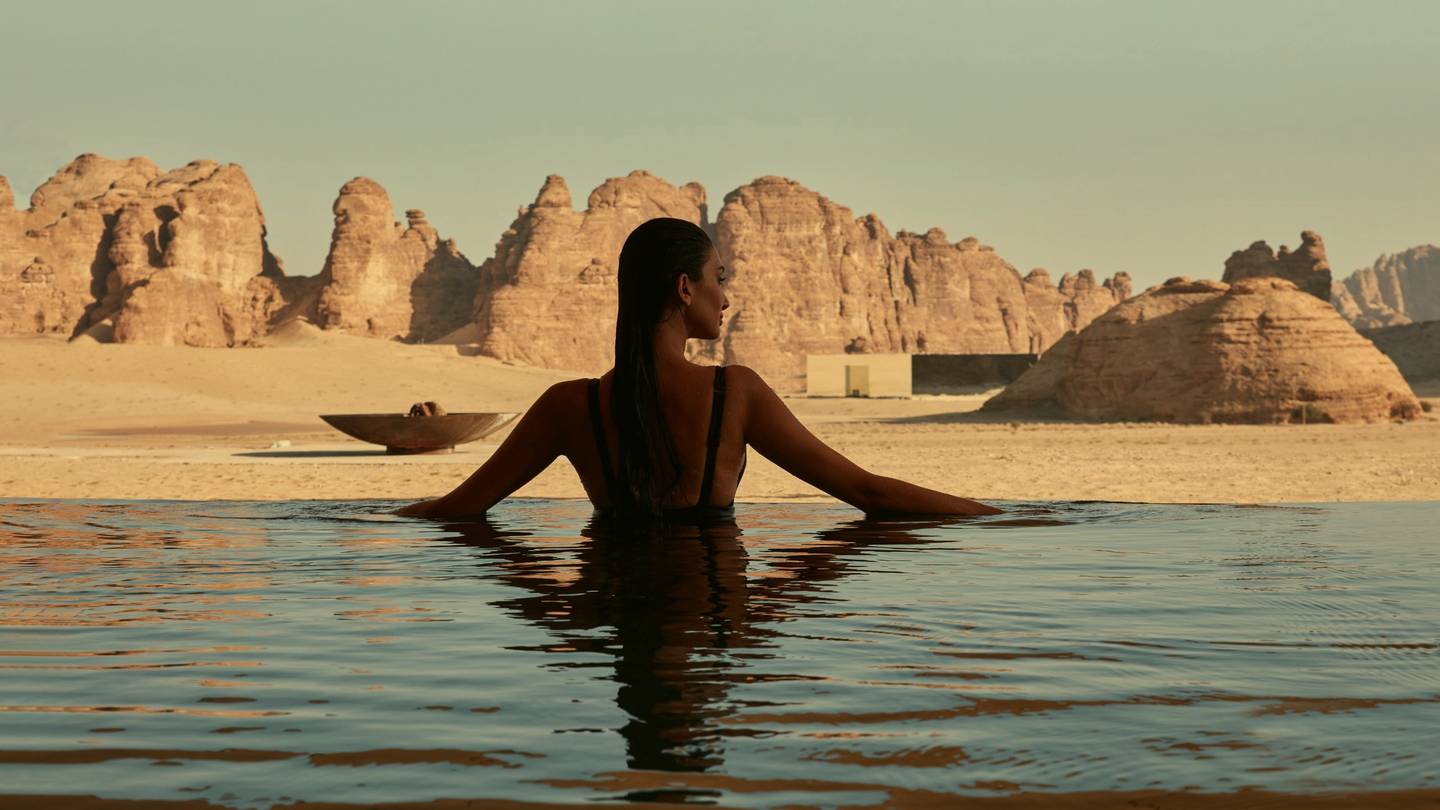 A guest in a desert infinity pool facing sandstone cliffs