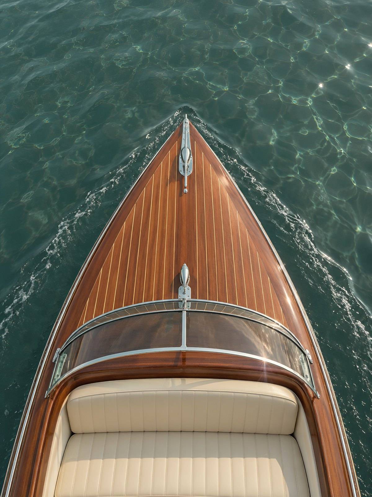 Overhead view of a varnished wooden boat bow cutting through calm water